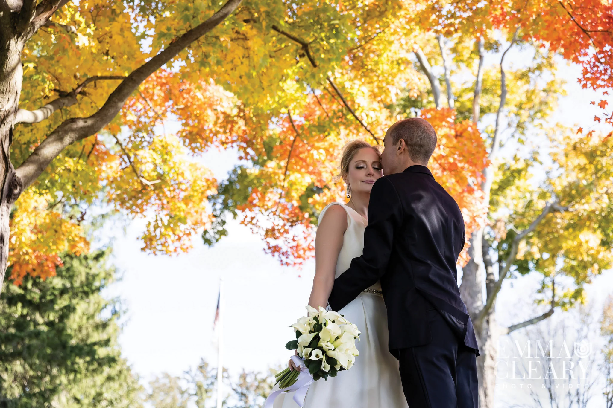 A couple, bride and groom, embracing under a tree in the fall at a beautiful wedding venue in Florham Park, NJ.