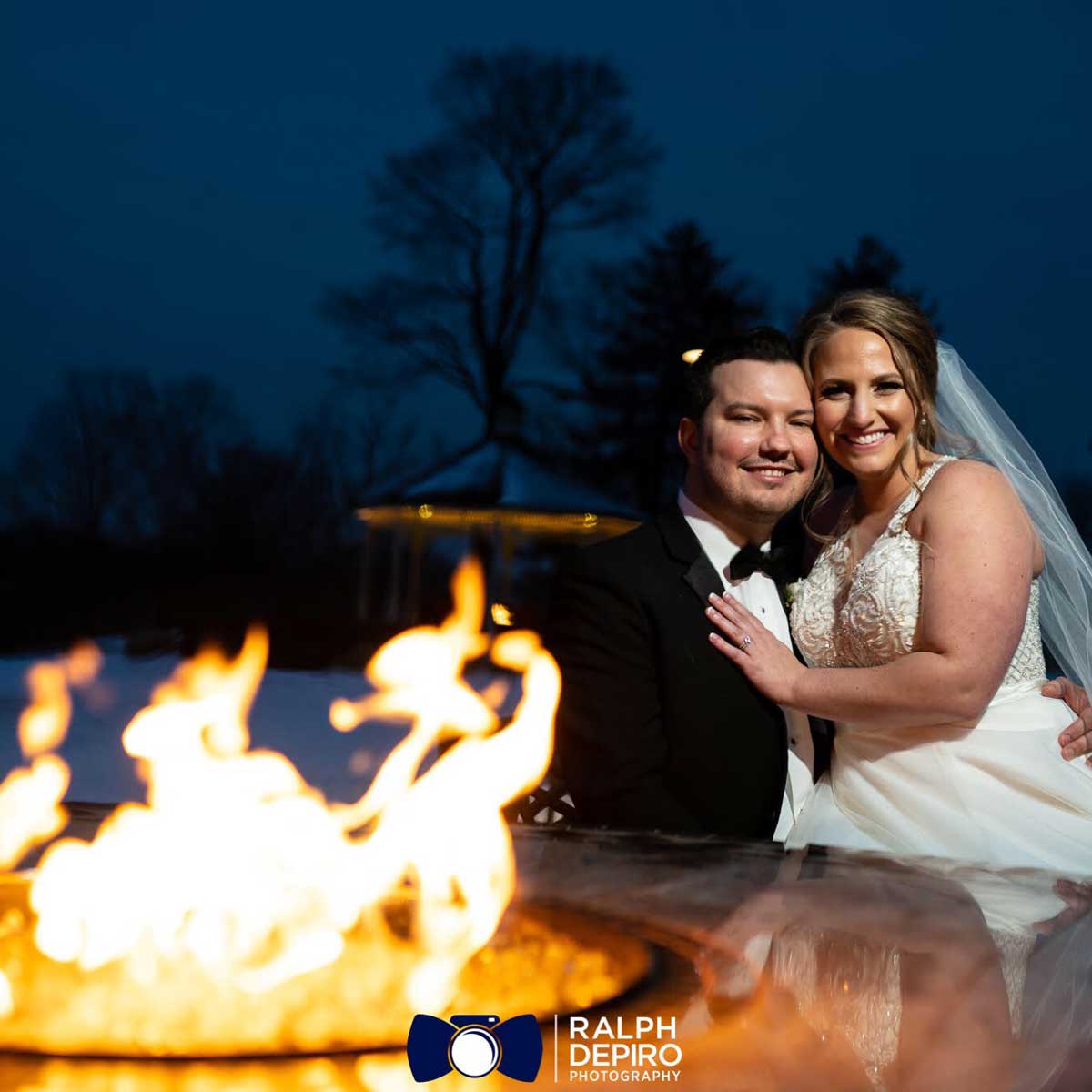 A bride and groom pose in front of a fire pit at one of the outdoor wedding venues in NJ.